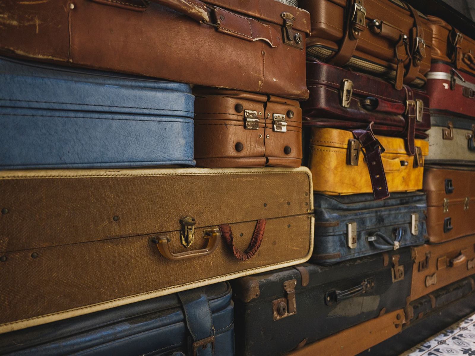 A collection of colorful, worn vintage suitcases stacked together, ideal for decor or trav