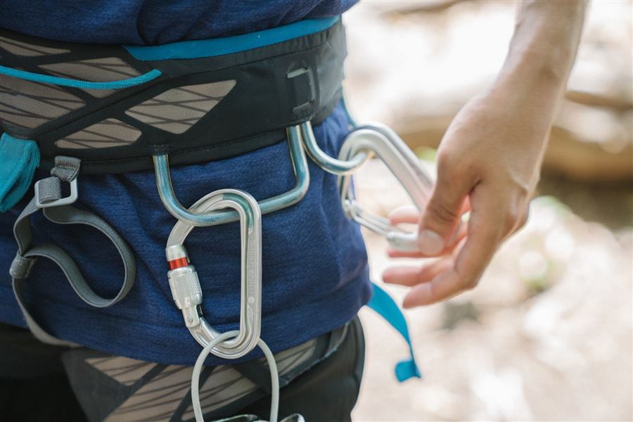 Detailed view of a person's climbing harness with carabiners and hand adjusting the setup.
