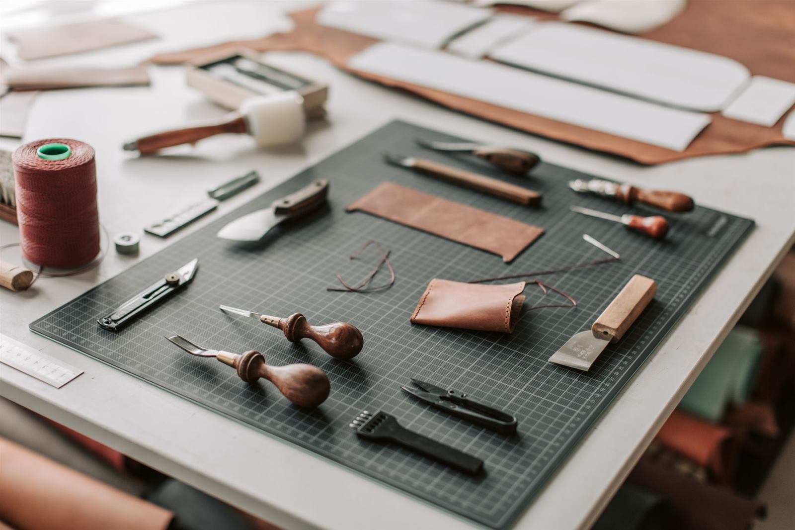 Close-up of leatherworking tools on a cutting mat in a workshop setting, showcasing crafts